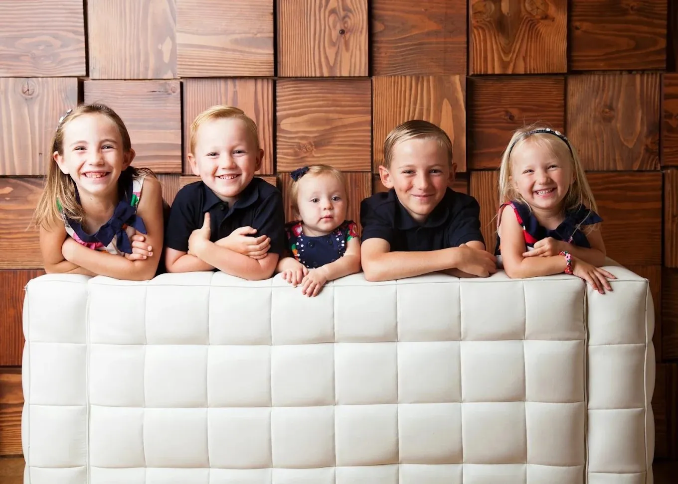 Five smiling children leaning on a white couch